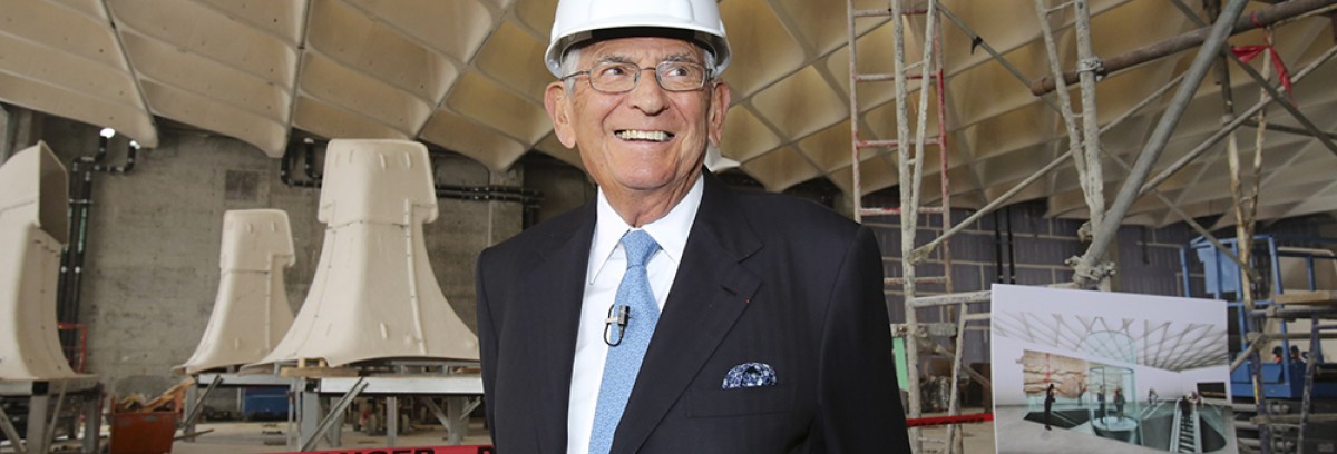 Eli广泛wearing a white hard hat and a dark suit standing at the construction site for The Broad Museum